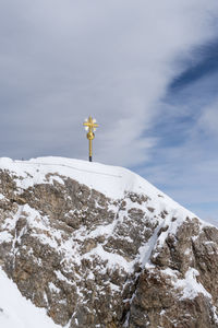Cross on snow covered mountain against sky