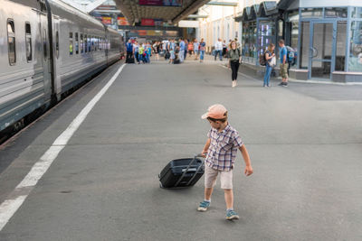 Full length of boy pulling luggage at railroad station platform