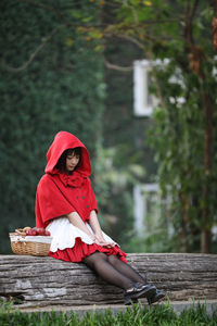 Young woman with fruits in basket looking away while sitting against tree