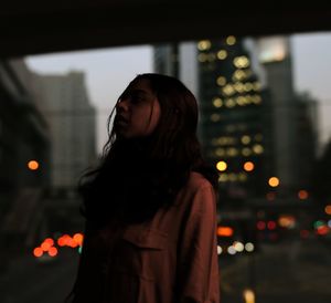 Young woman looking away while standing in city at night