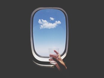 Close-up of hand holding glass of water in front of airplane window