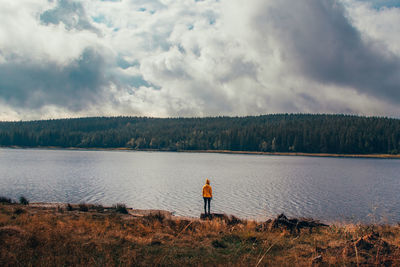 Rear view of man standing by lake against sky