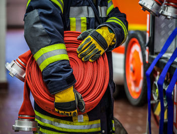 Midsection of firefighter holding hose at fire station