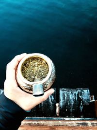 Cropped hand of person holding marijuana in container over lake