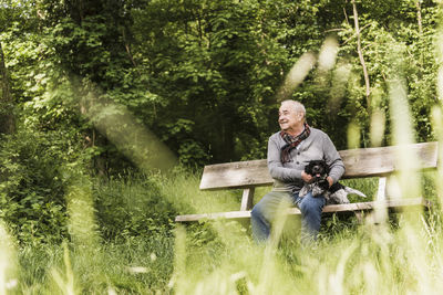 Smiling senior man sitting with his dog on a bench in nature