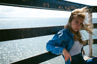 Young woman sitting on pier over sea against sky