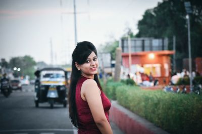 Portrait of young woman standing by car against sky