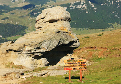 Rock formation with information sign on field at bucegi natural park