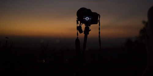 Silhouette of camera on field against sky during sunset