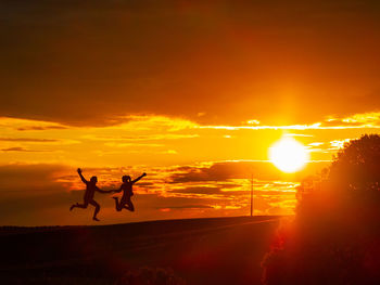 Silhouette people jumping against orange sky during sunset