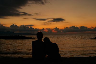 Silhouette couple sitting against orange sky during sunset