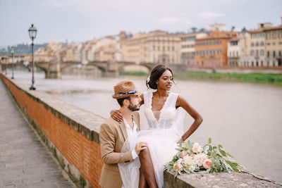 Couple holding umbrella on bridge against buildings