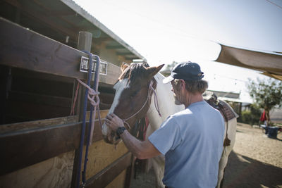 Rear view of man standing by horse at ranch