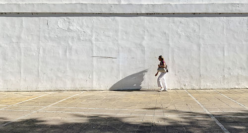 Full length of woman standing on footpath against wall