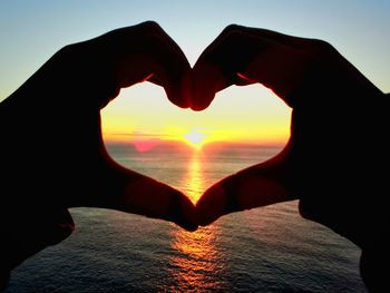 Close-up of hand holding heart shape against sea during sunset