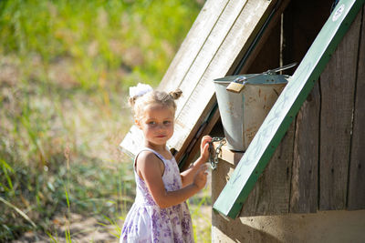 Surprised pretty little girl in country style staying near to well.