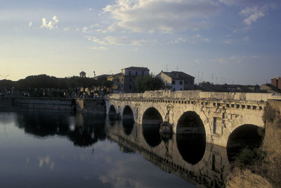 Arch bridge over river against sky in city