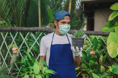 Botanist wearing mask holding potted plant at shop