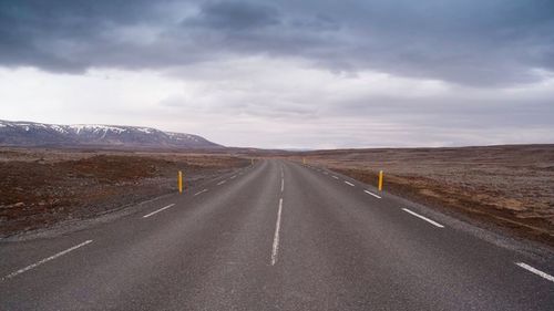Empty road by mountains against cloudy sky