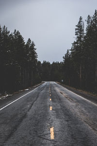 Empty road along trees and against sky