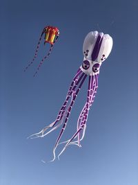 Low angle view of kites flying against clear blue sky