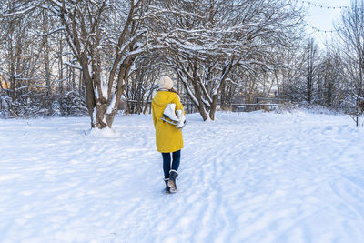 Young woman in yellow jacket with ice skates walking through snowy park