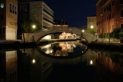 Illuminated bridge over river by buildings in city at night