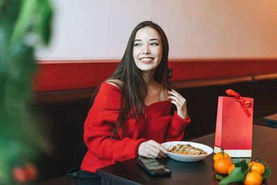 Smiling young woman holding drink sitting on table