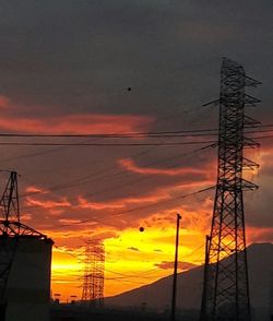 Silhouette electricity pylon against dramatic sky during sunset