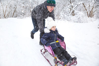 Dad takes his little daughter on a sledge uphill through the winter snow forest. active 
