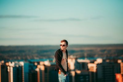 Portrait of young man wearing sunglasses standing against cityscape