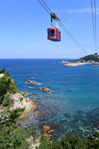 Overhead cable car over sea against blue sky