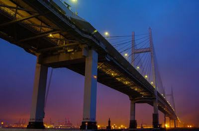 Low angle view of suspension bridge at night just before sunrise on a foggy morning in japan.