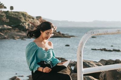 Young woman looking at camera on beach against sky