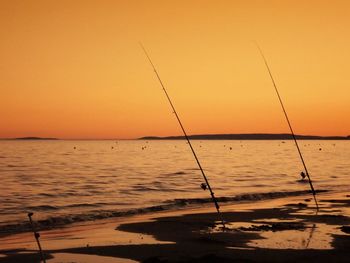 Fishing rods on shore at beach against sky during sunset