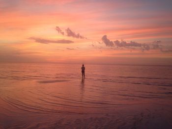 Silhouette teenage girl standing in sea against sky during sunset