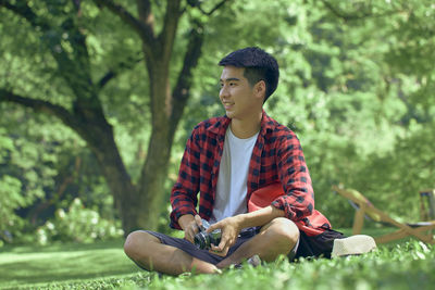 Young man looking away while sitting on tree