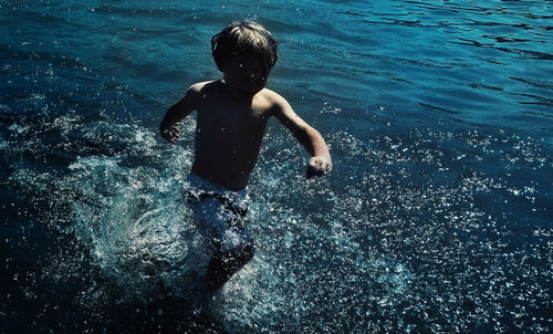 Shirtless boy wading in sea
