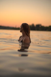 Side view of shirtless boy swimming in sea during sunset