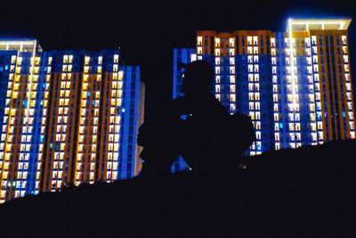 Rear view of silhouette man standing against illuminated building