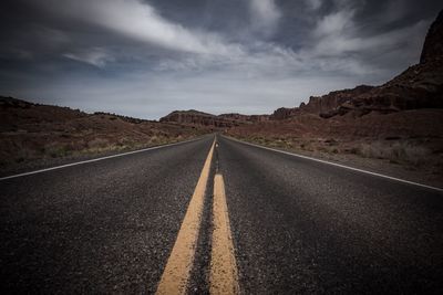 Empty road leading towards rocky mountains against sky
