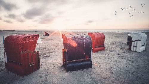 Hooded chairs on beach against sky during sunset