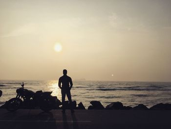 Silhouette people standing on beach against sky during sunset