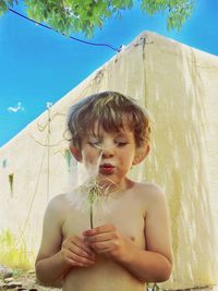 Shirtless boy blowing dandelion seeds in back yard