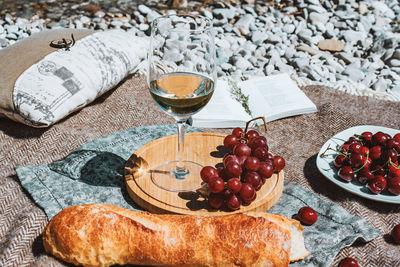 Summer romantic rustic picnic on the beach, white wine glass, baguette, cherries, grape, open book