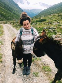 Full length of woman standing with donkeys on walkway against mountains