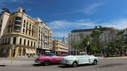 Cars on road by buildings against blue sky