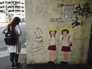 Rear view of backpack woman standing graffiti on concrete wall