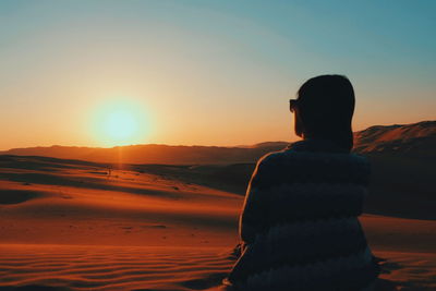 Rear view silhouette of woman looking at sunset while standing at desert