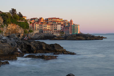 Sea by buildings against sky during sunset